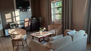 Un salon comprenant un canapé, deux fauteuils en osier, une table basse, un téléviseur à écran plat, un four à micro-ondes et un petit meuble.