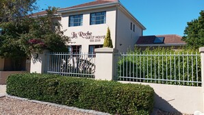 A two-story building with a beige facade, a red-tiled roof, and a sign reading "La Roche Guest House." - La Roche Guest House (Cape Town)