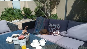 An outdoor seating area with a table set for breakfast, including a drink, a fruit, and a hat. - La Roche Guest House (Cape Town)