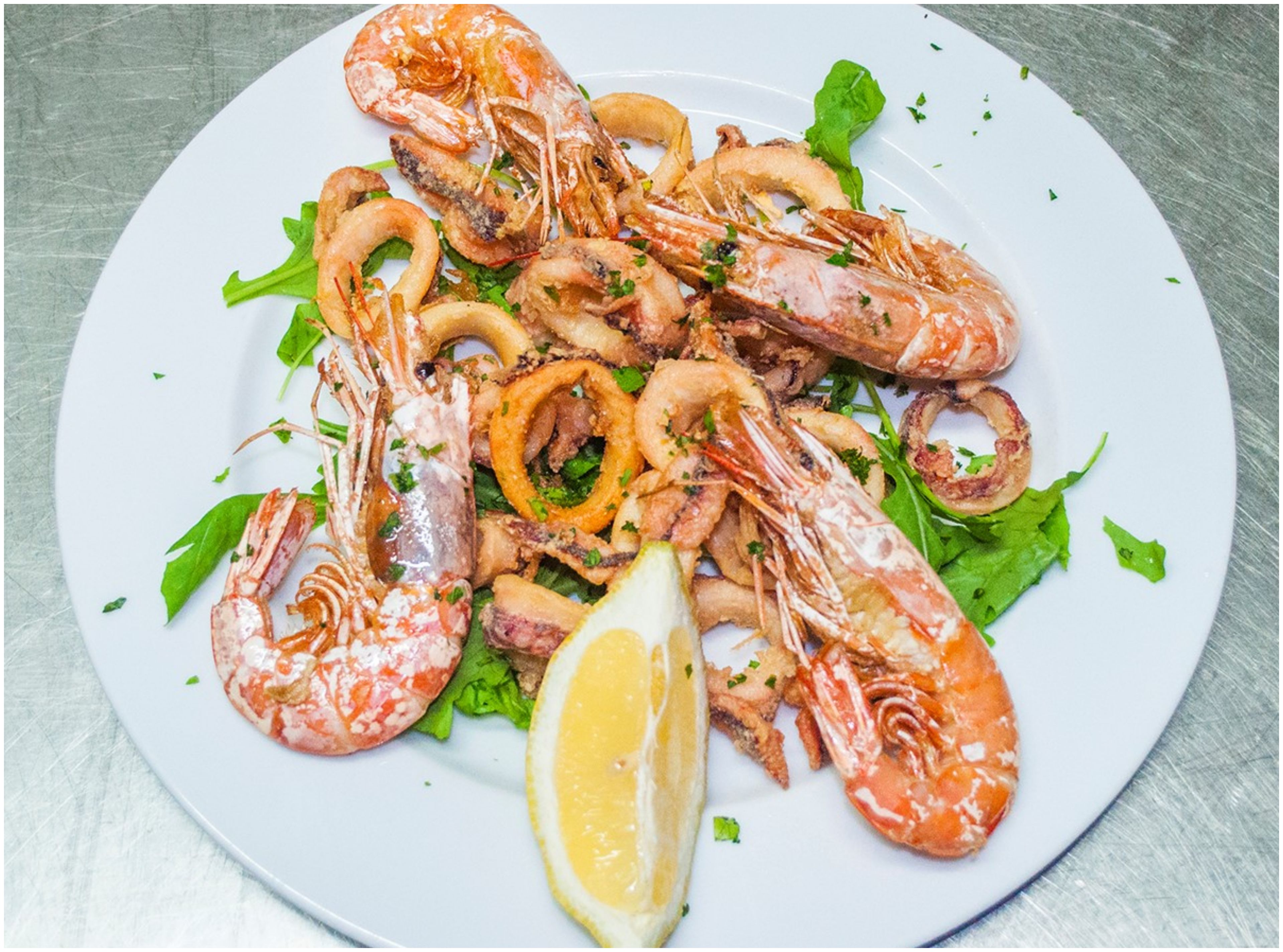 Une assiette de fruits de mer cuits, comprenant des crevettes et des anneaux de calamars, garnie de persil et d’une tranche de citron.