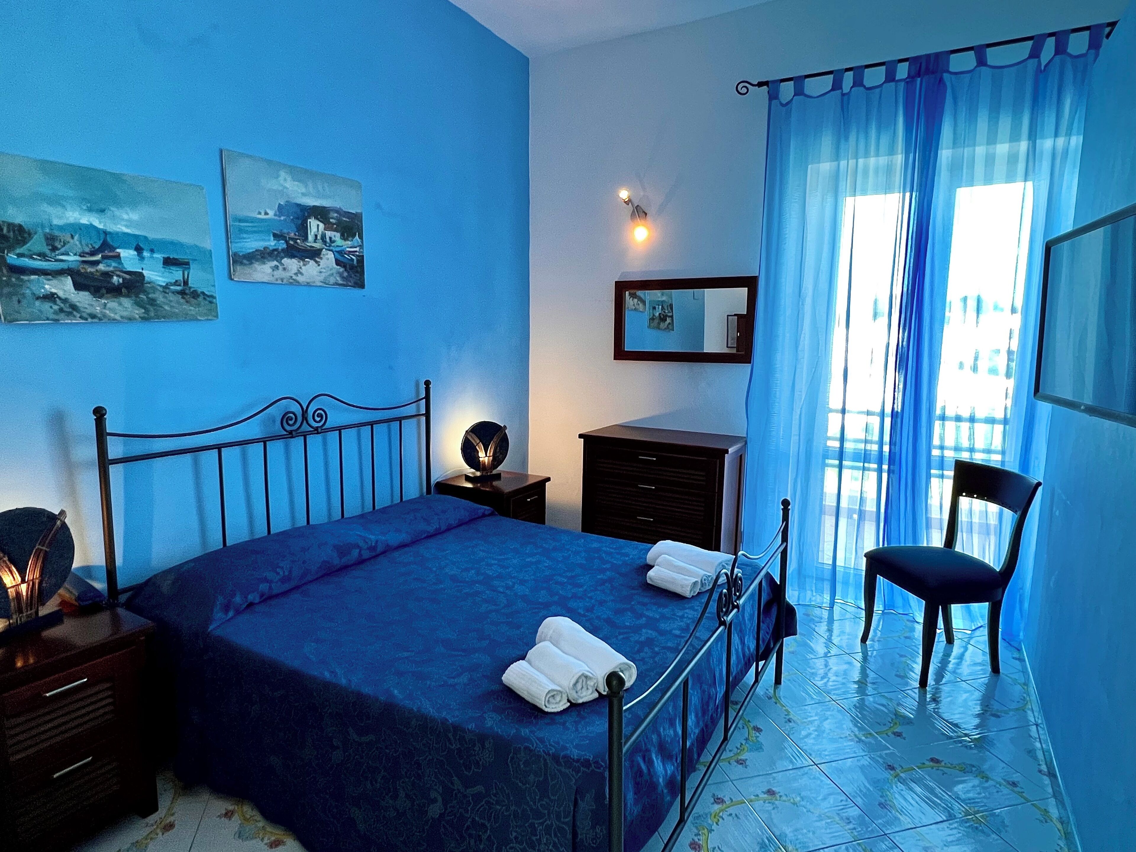 A bedroom with a bed, a chair, a dresser, a nightstand, a lamp, and two paintings on the wall.