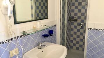 Une salle de bain avec un lavabo blanc, une étagère en verre, une douche bleue et un sèche-cheveux fixé au mur.