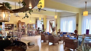 A spacious living area with a dining table, wicker furniture, and a large window with curtains. - Hotel Ortensia (Ponza)