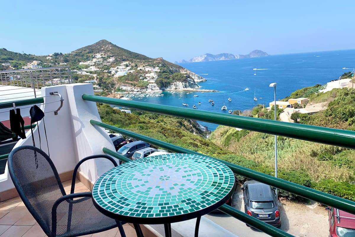Un balcon avec une table et des chaises, donnant sur une zone côtière avec des bateaux et des bâtiments.