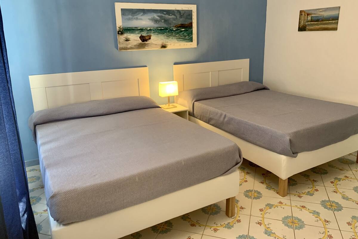 Une chambre avec deux lits simples, une table de chevet avec une lampe et un tableau représentant un bateau sur la mer.