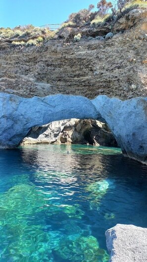 A natural rock formation with a clear blue pool beneath it.