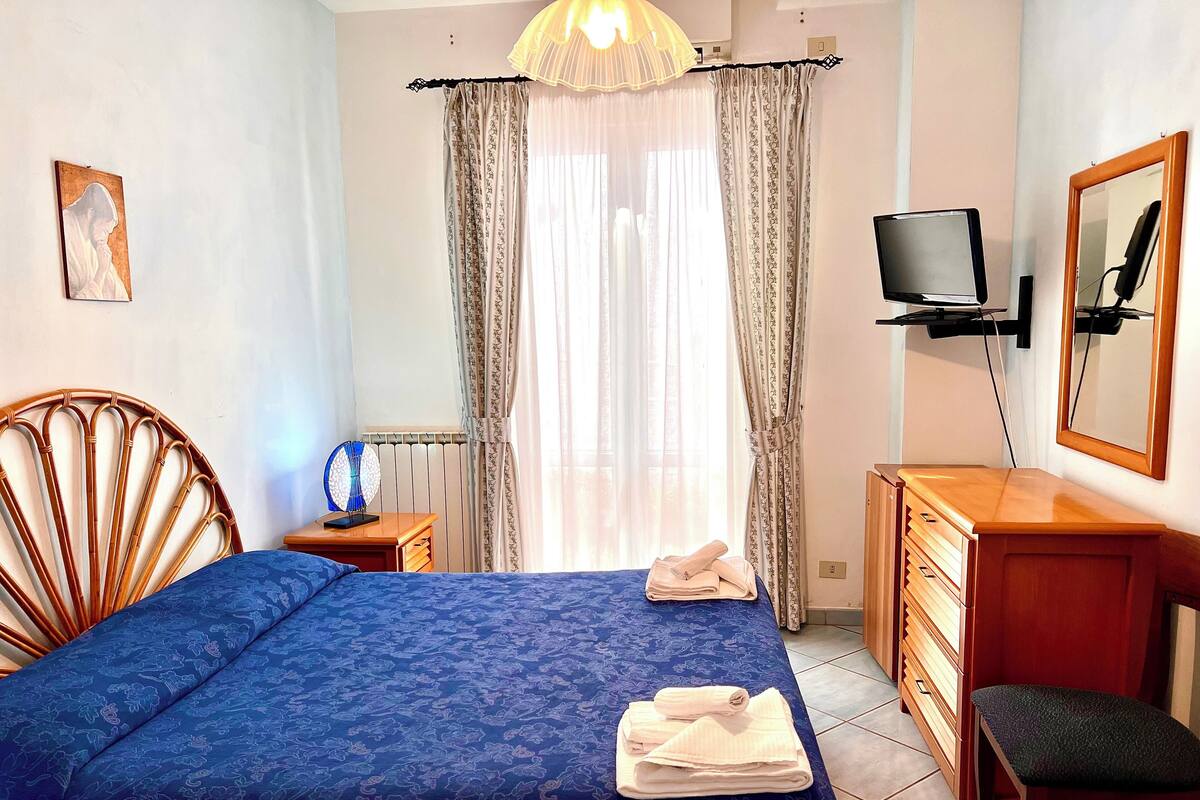 Une chambre d’hôtel avec un lit, une chaise en bois, un bureau avec une télévision et un miroir.