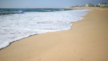 Una playa con olas, un muelle y edificios al fondo.