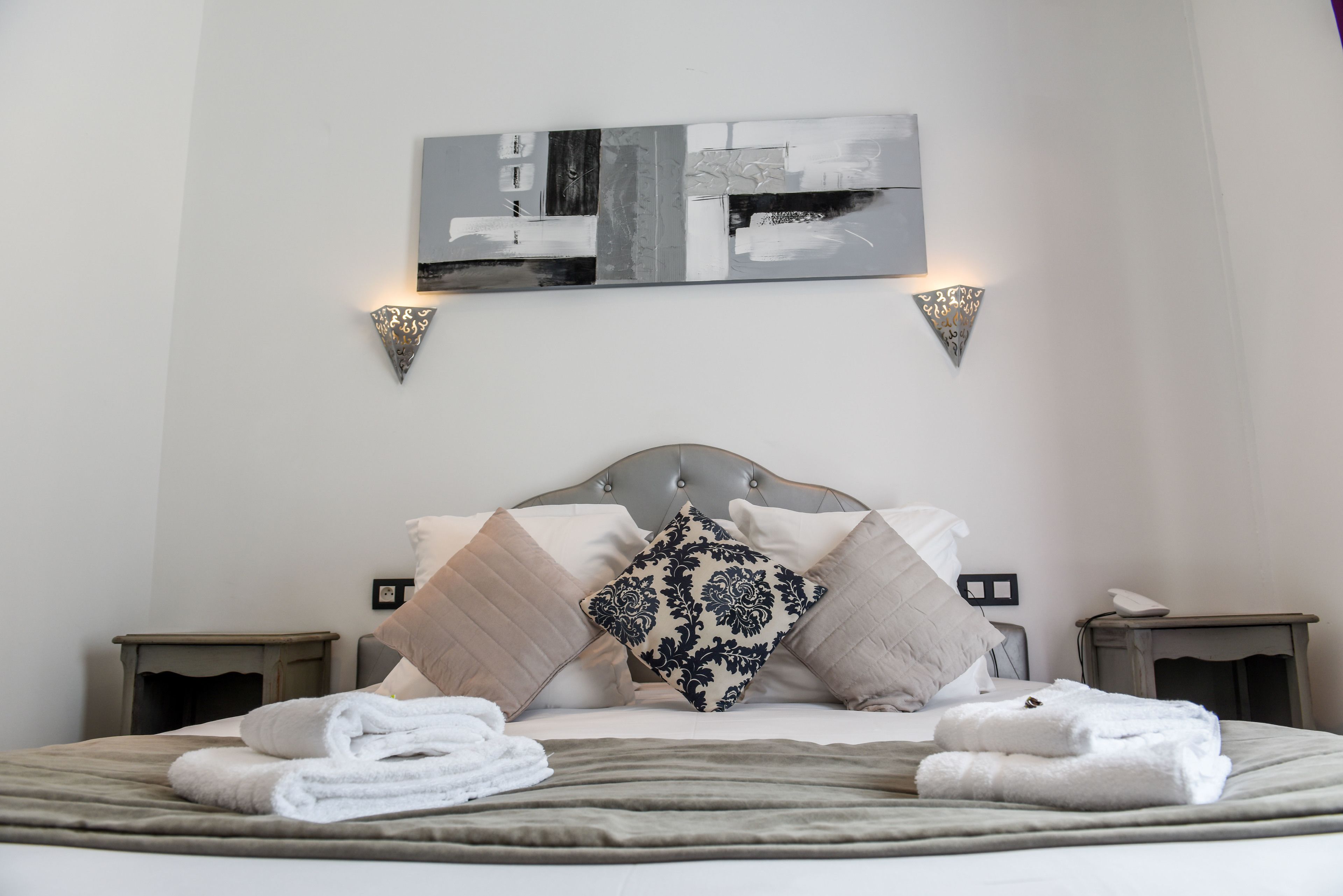 A neatly made bed with pillows and towels, a wall-mounted abstract painting, and two wall sconces.