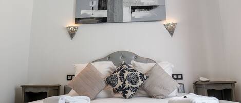 A neatly made bed with pillows and towels, a wall-mounted abstract painting, and two wall sconces.