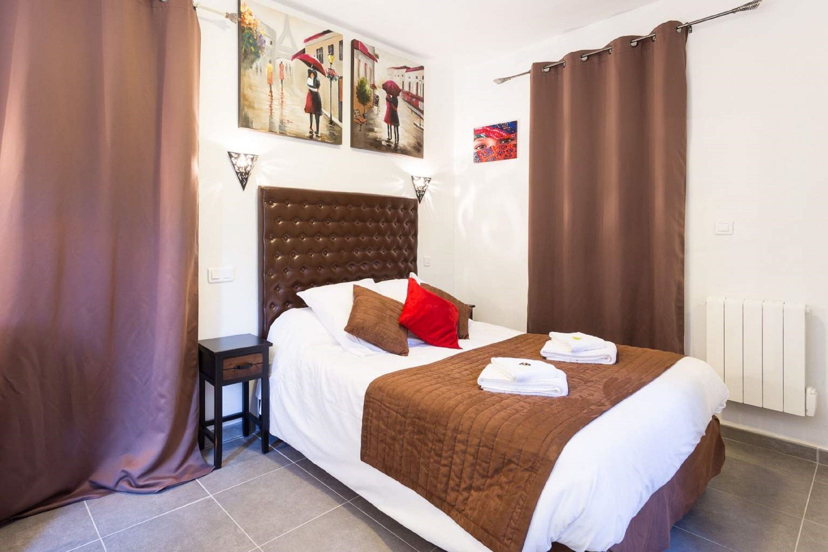A hotel room with a large bed, brown curtains, a headboard, and artwork on the walls.