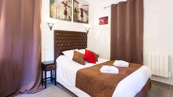 A hotel room with a large bed, brown curtains, a headboard, and artwork on the walls.