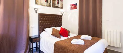 A hotel room with a large bed, brown curtains, a headboard, and artwork on the walls.