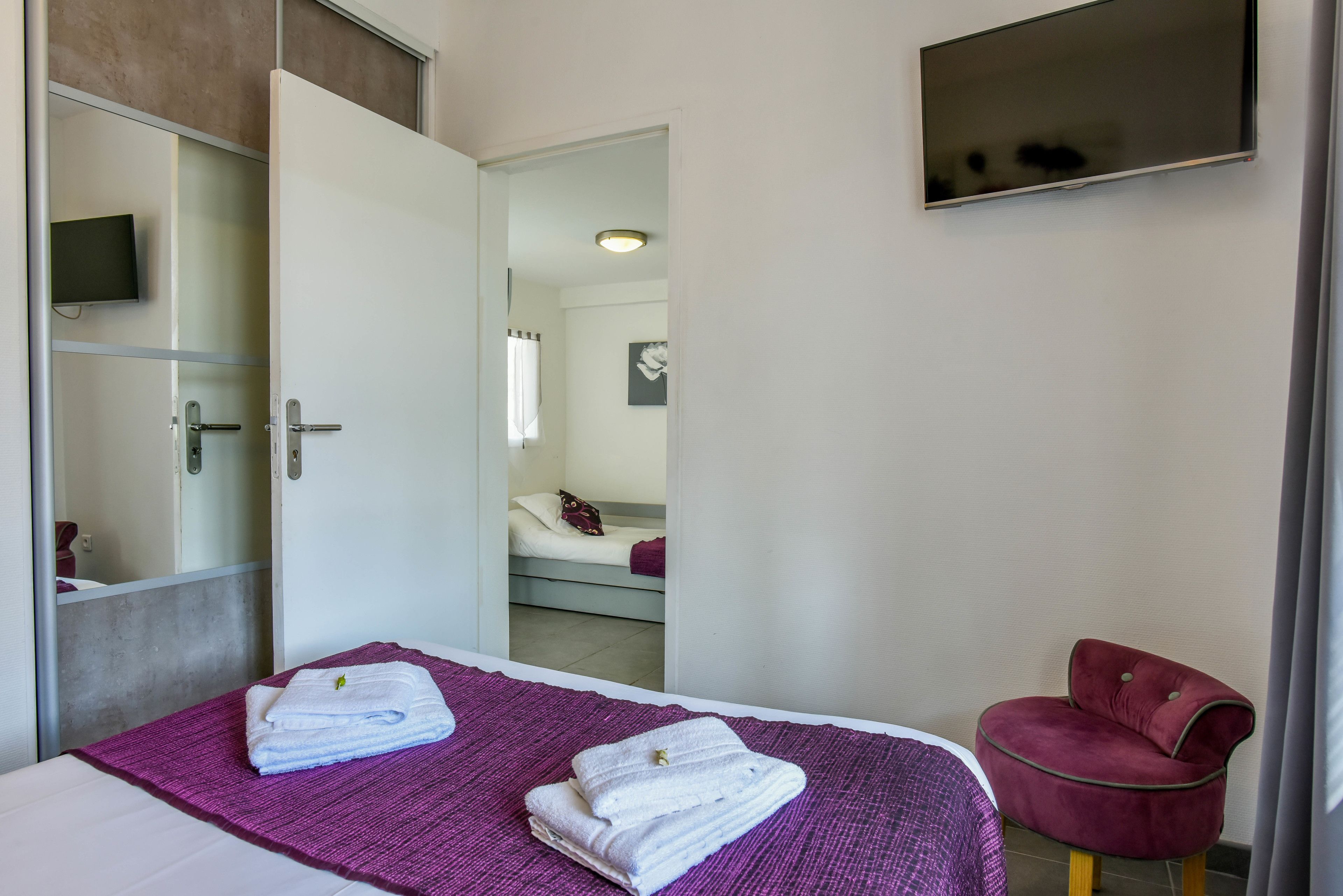 A hotel room with a bed, a chair, a TV, and a bathroom visible through an open door.
