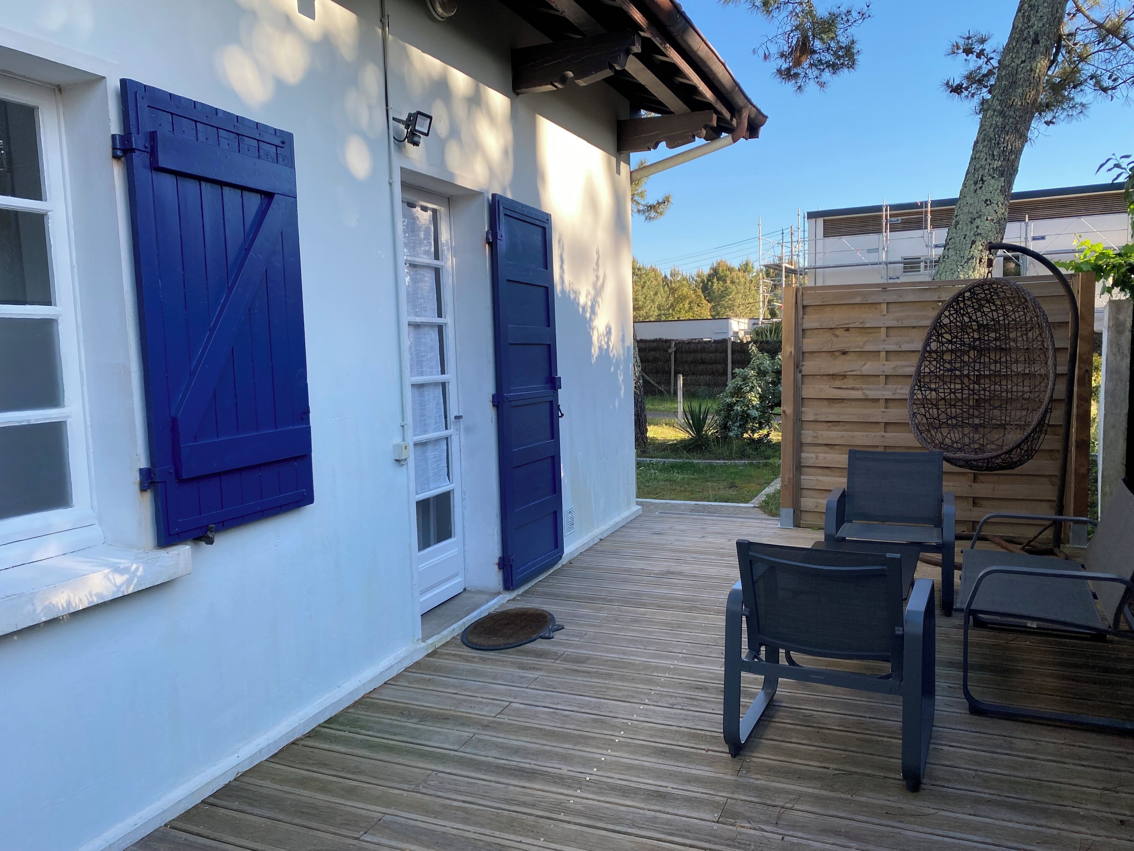 A wooden deck with outdoor furniture, a covered seating area, and a view of a building with blue shutters and a security camera.