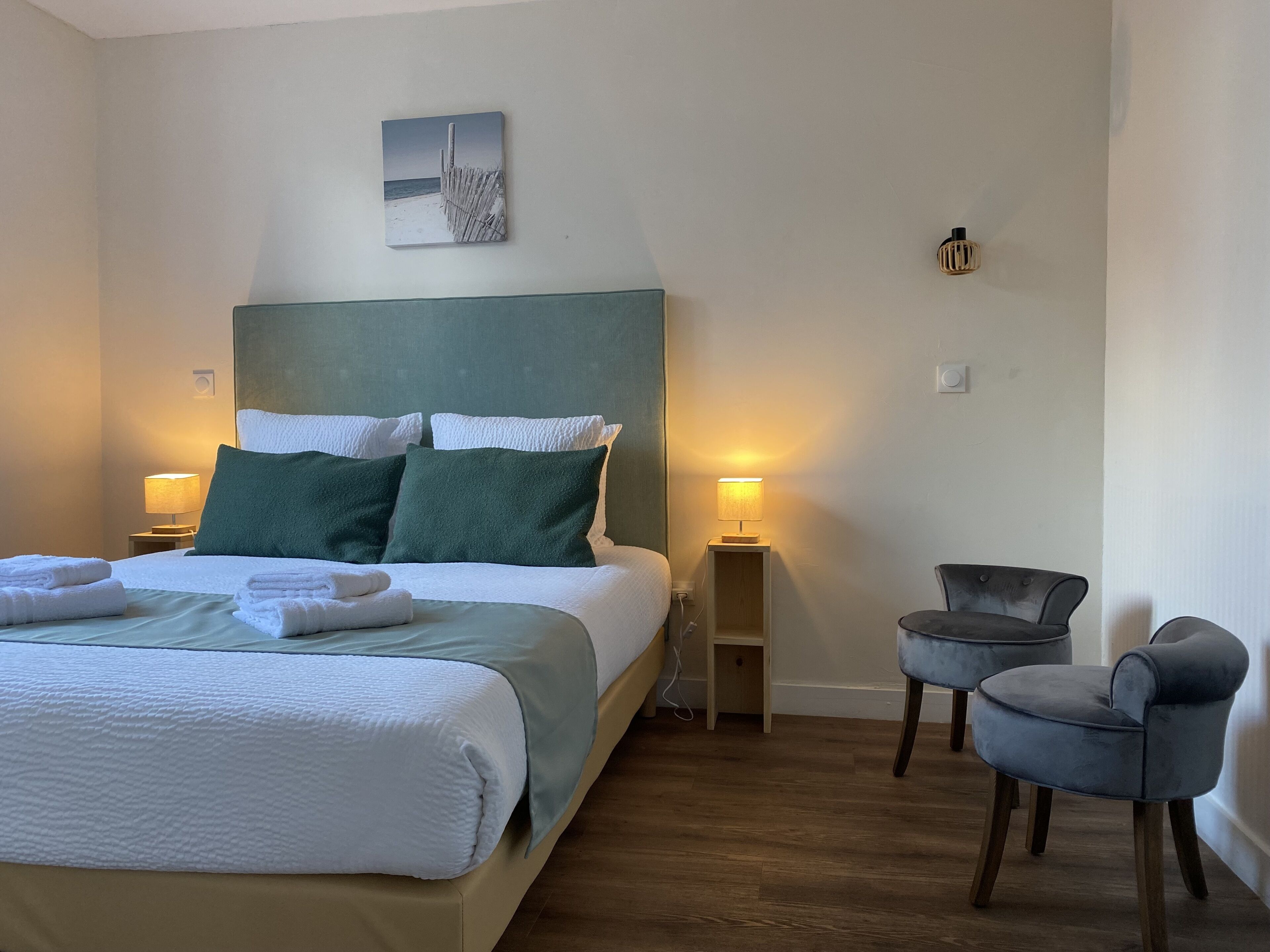Une chambre d’hôtel avec un lit, deux lampes de chevet, une petite table, deux chaises et un tableau au mur.