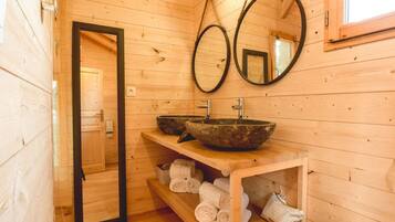 Un baño de cabaña de madera con dos lavamanos de piedra, un espejo y estantes con toallas.