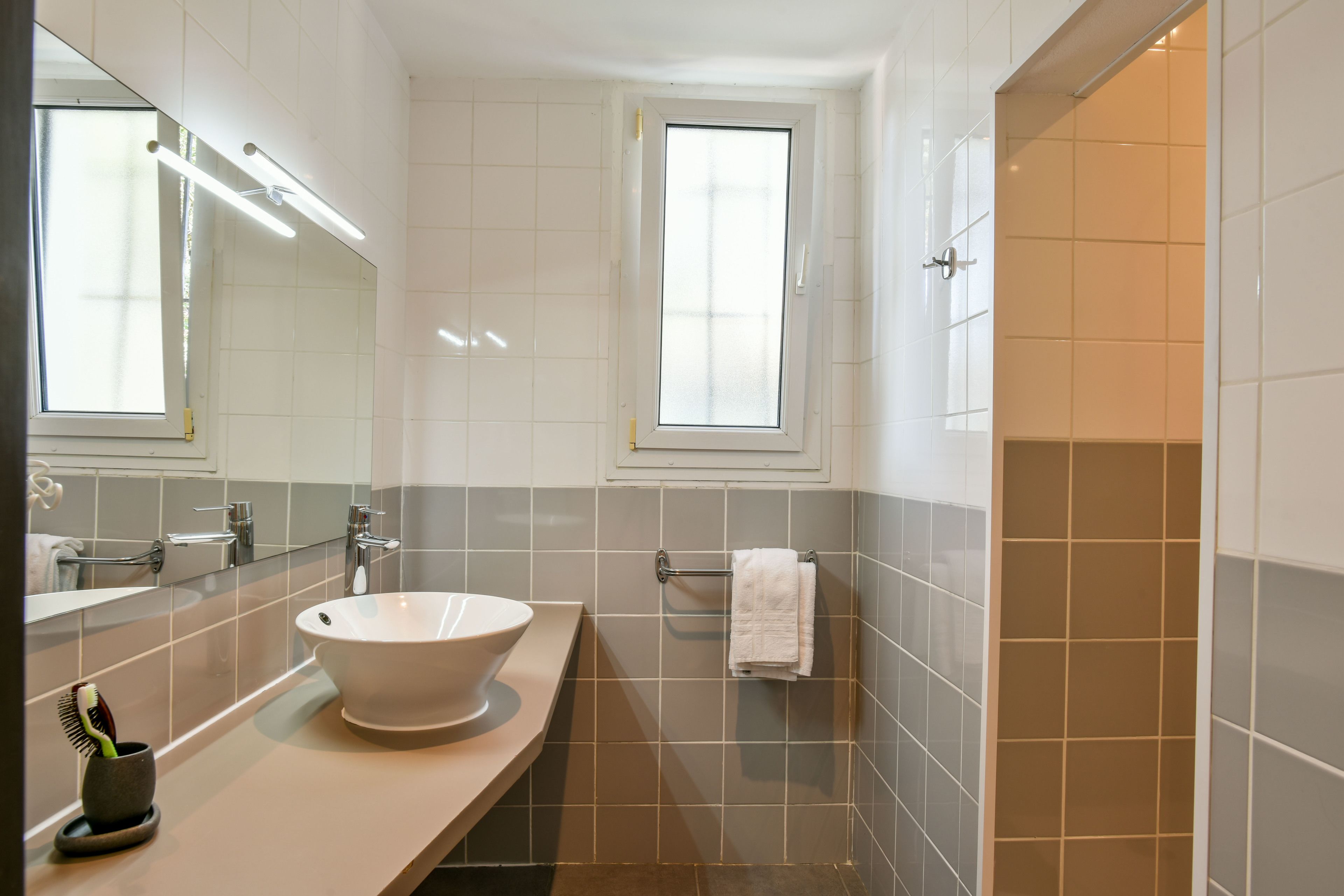Une salle de bain moderne avec un grand miroir, un lavabo blanc et une fenêtre.