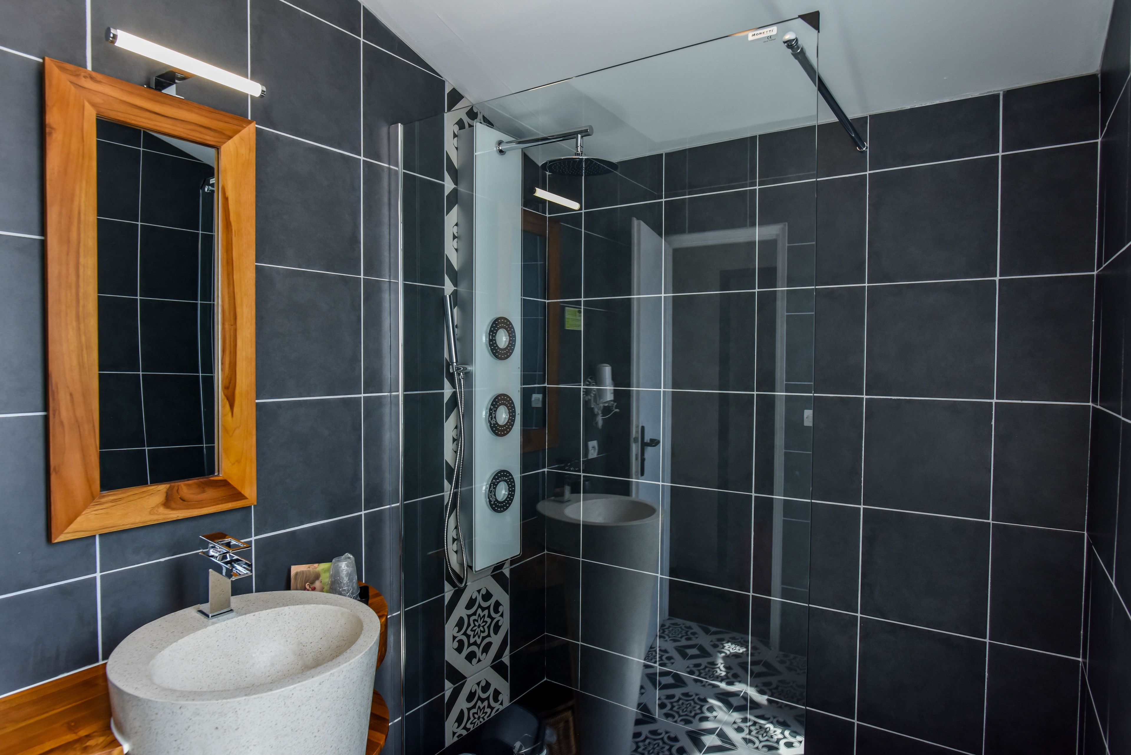 Un baño moderno con un espejo grande, un lavamanos independiente y una zona de ducha.