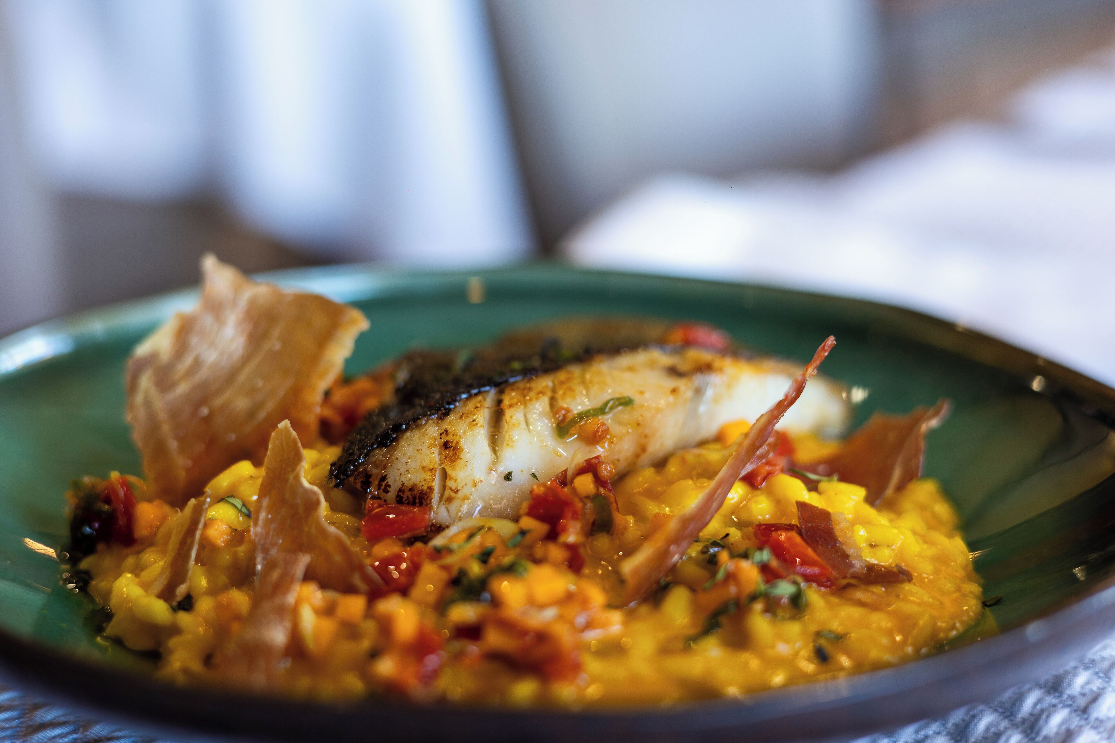 A plate of food with a piece of fish, vegetables, and a garnish.