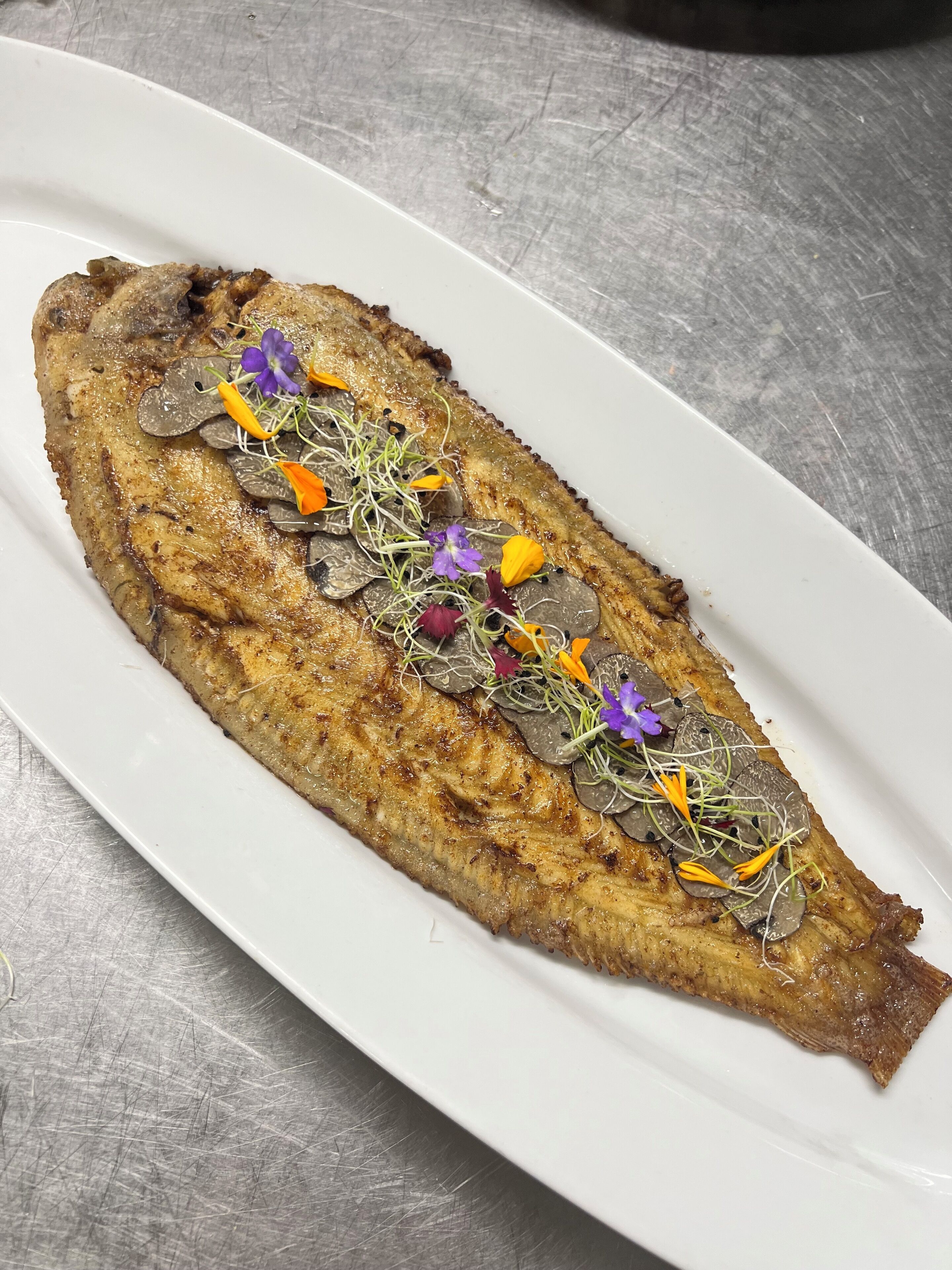 A white plate with a grilled fish garnished with edible flowers and herbs.