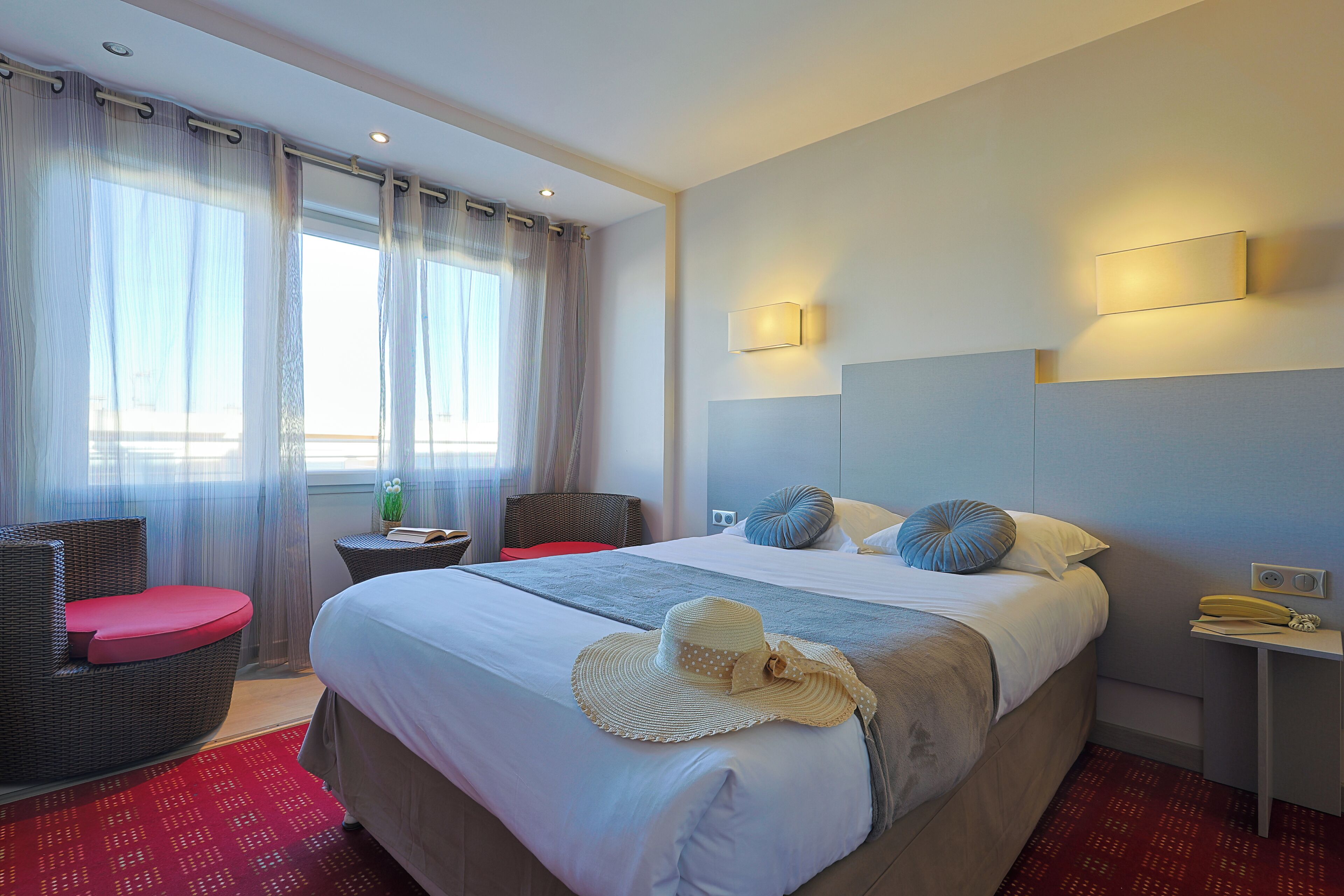 A hotel room with a bed, a chair, a nightstand, and a window with curtains.