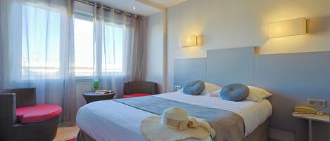 A hotel room with a bed, a chair, a nightstand, and a window with curtains.