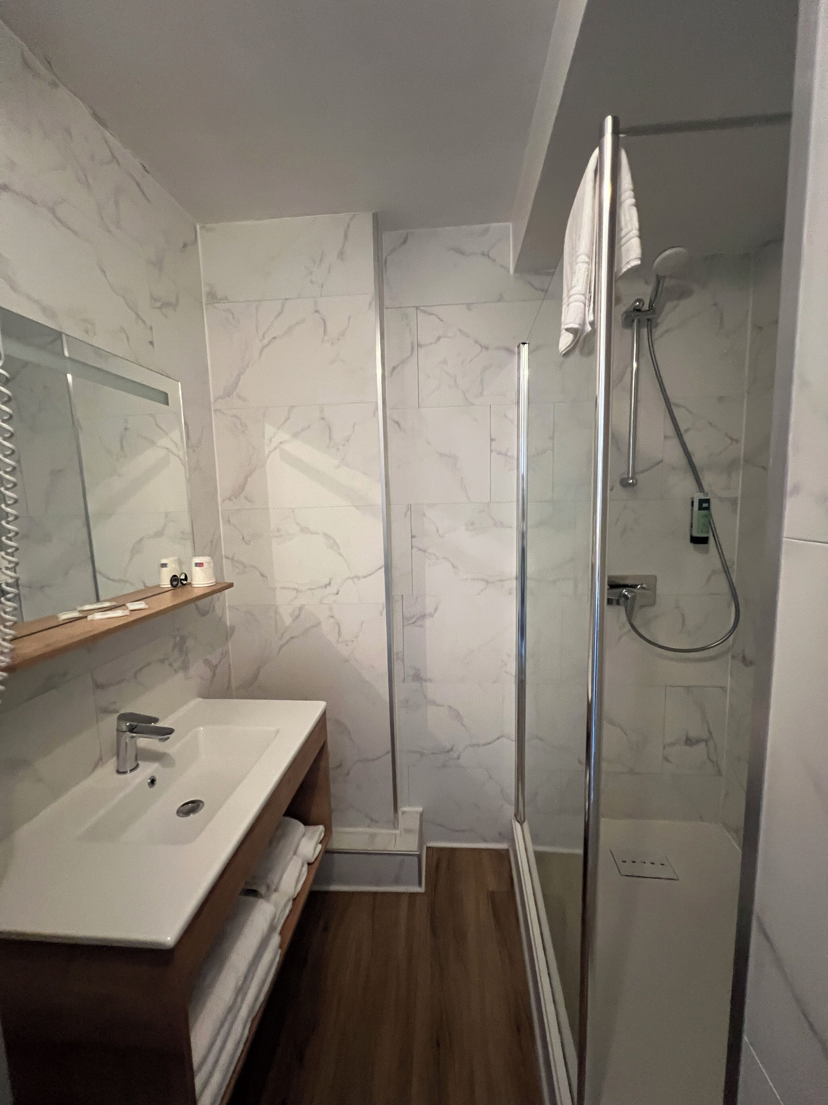 A modern bathroom with a glass-enclosed shower, a wooden vanity, and marble walls.