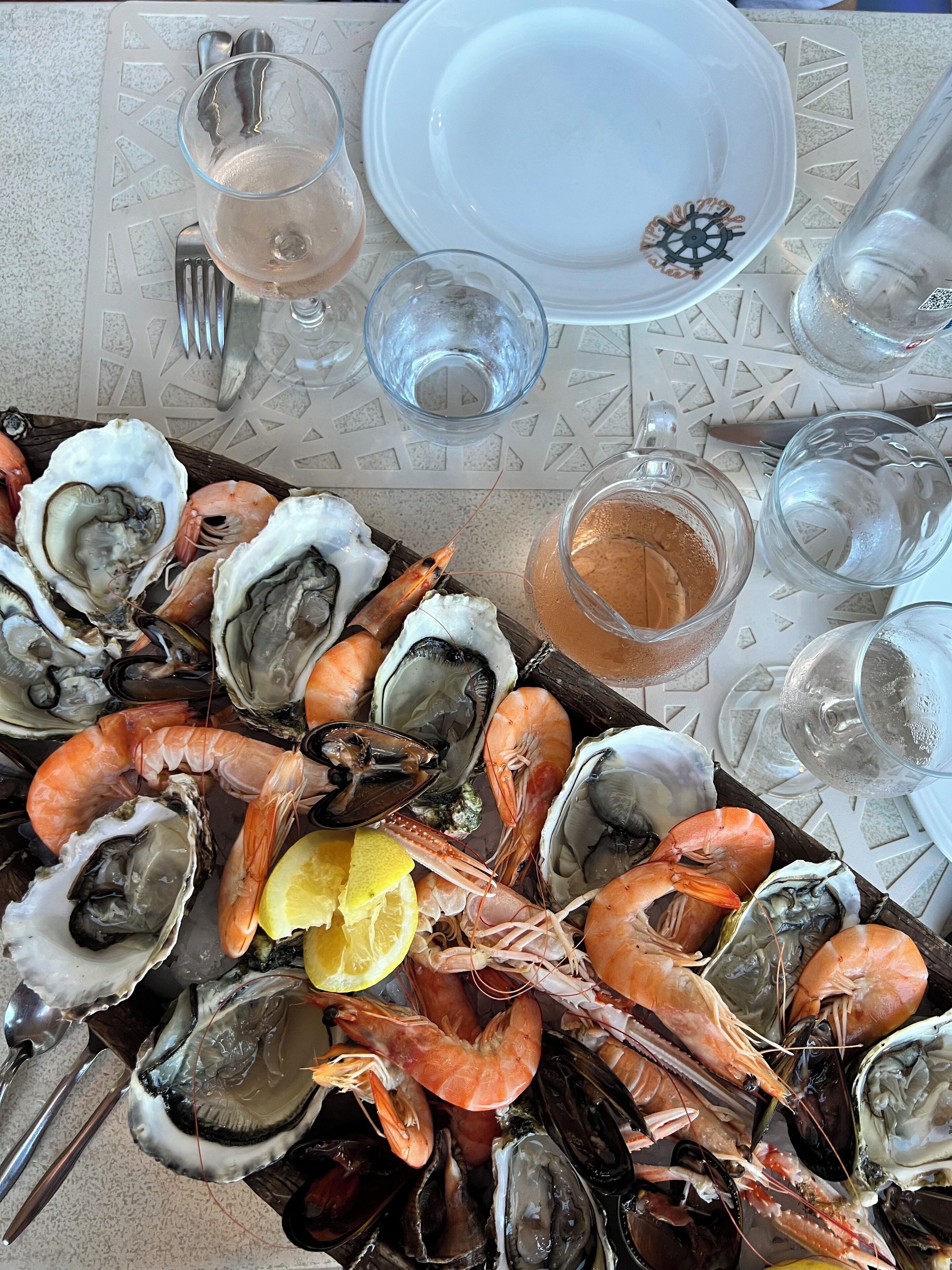 A seafood platter with oysters, shrimp, and mussels, accompanied by a glass of wine and a lemon wedge.