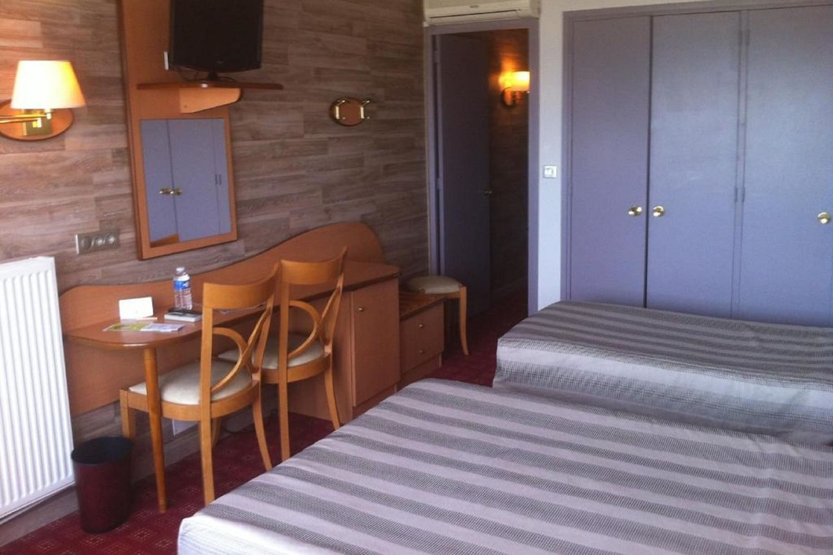 Ein Hotelzimmer mit zwei Betten, einem Schreibtisch mit Stuhl, einem Fernseher und einem Kleiderschrank.