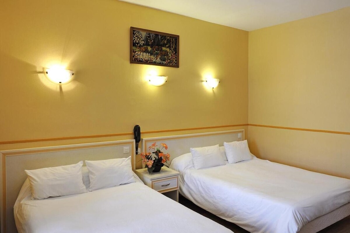 Une chambre d’hôtel avec deux lits, une table de chevet avec un téléphone et un vase de fleurs, et des lampes fixées au mur.
