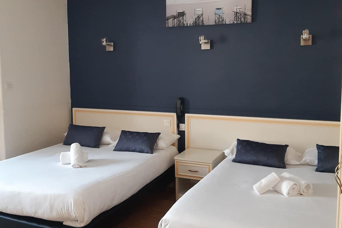 Habitació d'hotel amb dos llits, cadascun amb roba de llit blanca i naxes fosques, una petita taula de nit amb una làmpada i un quadre penjat a la paret.