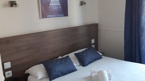 Quarto de hotel com uma cama grande, duas almofadas, cama bem arrumada, um quadro na parede e uma mesa de cabeceira com abajur.