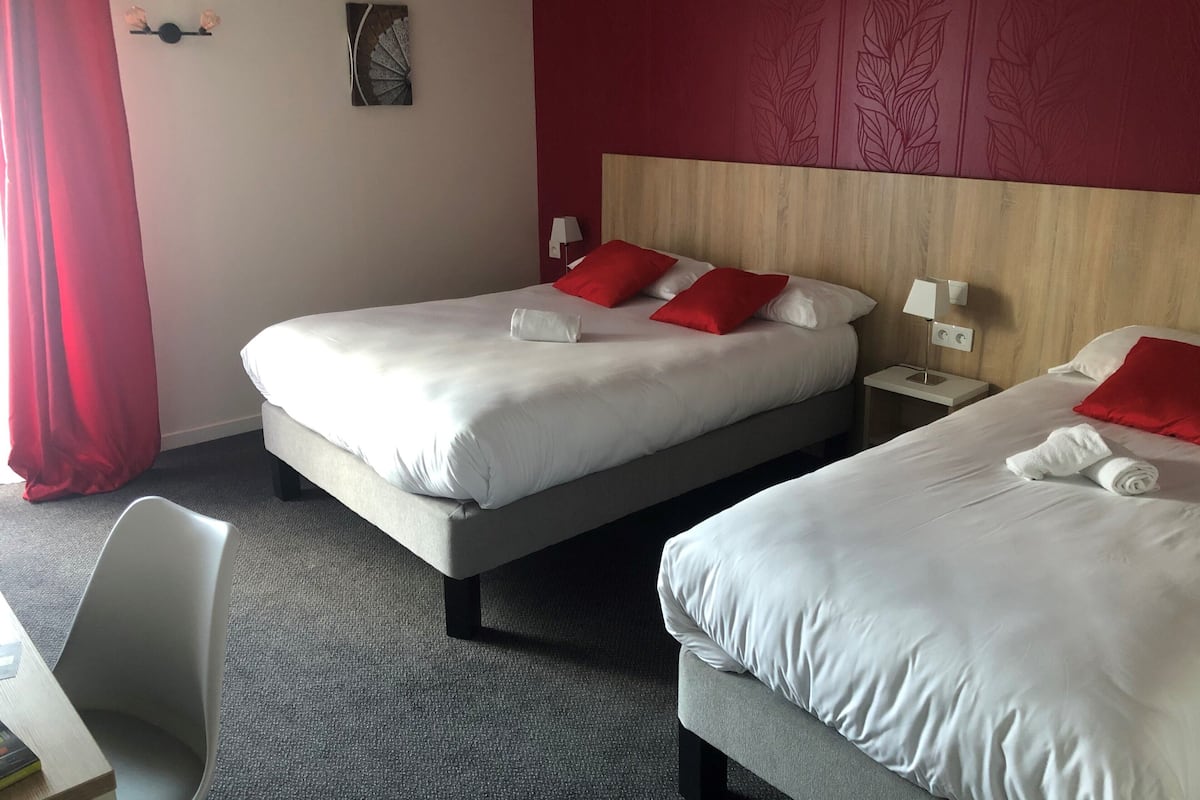 Habitació d'hotel amb dos llits, almoinades vermelles, una taula petita i una cadira.