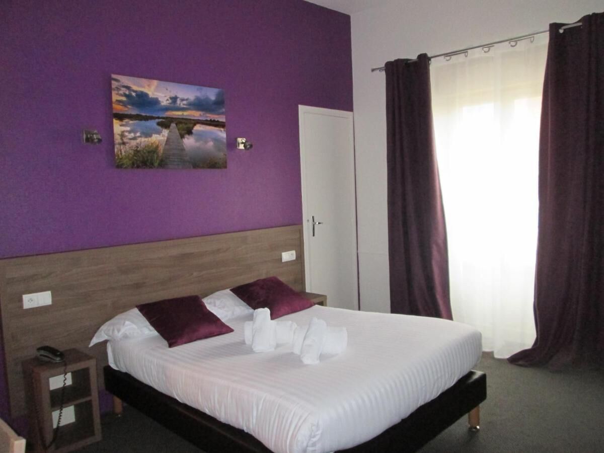 A hotel room with a bed, a nightstand, a painting on the wall, and a door.
