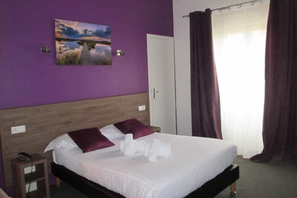 Habitació d'hotel amb un llit, una tauleta de nit, un quadre a la paret i una porta.
