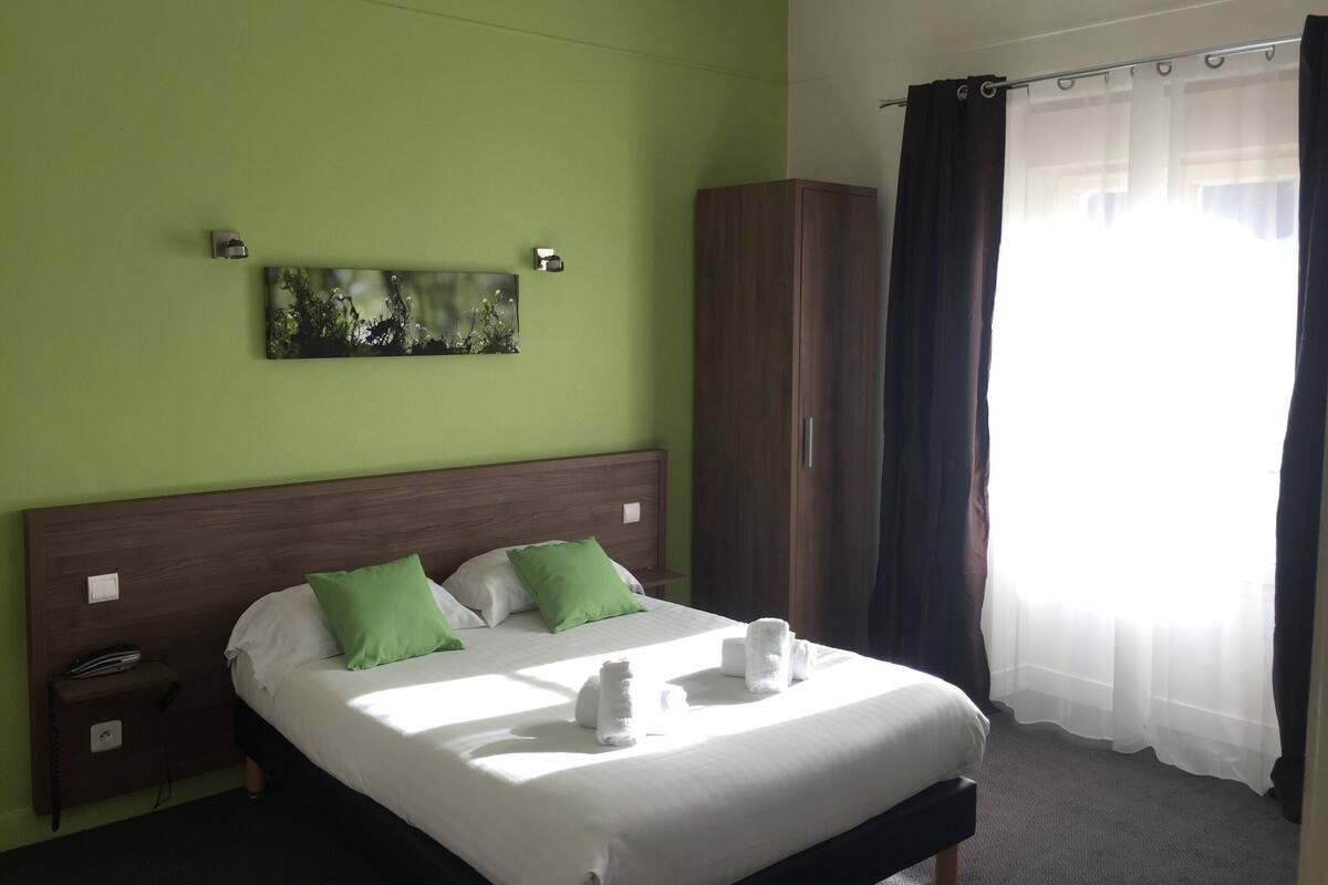 Habitació d'hotel amb llit, parets verdes, un quadre, un armari i una finestra amb cortines.