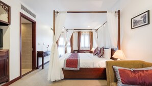A four-poster canopy bed with a red throw blanket, a wooden headboard, and a nightstand with a lamp.