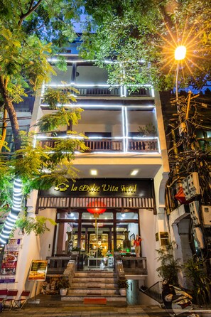 A multi-story building with balconies, a sign reading "La Dolce Vita Hotel," and outdoor seating with potted plants. - La Dolce Vita (Hanoi)