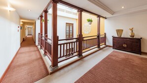 A hallway with a wooden railing, a carpeted floor, and a decorative wall with a plant.
