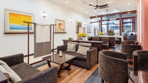 A modern hotel lobby with a wooden floor, comfortable seating, artwork on the walls, and a view of the city through large windows.