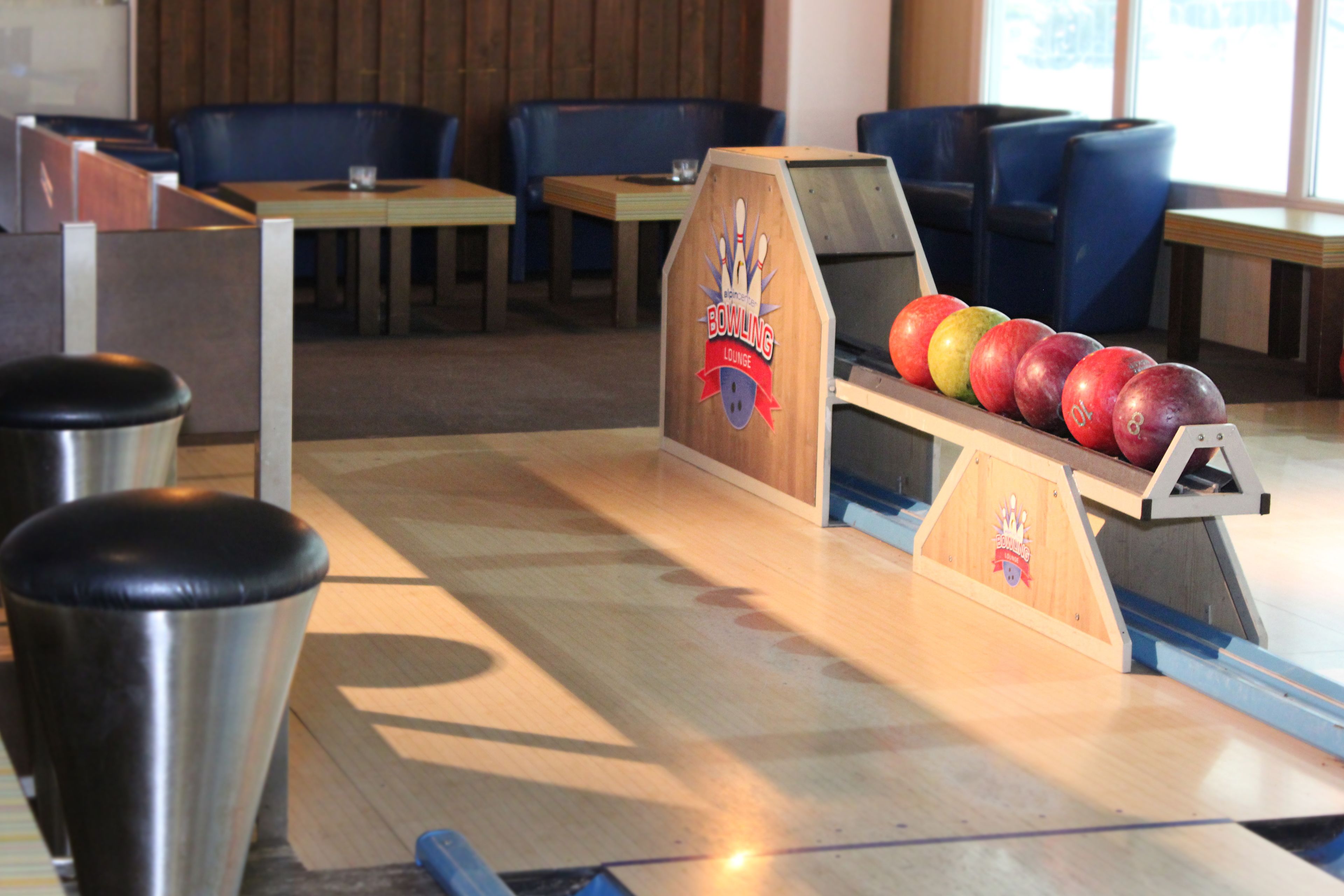 Una bolera con una pista de madera, un lanzador automático de bolos y varias bolas.
