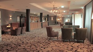 A spacious lobby with a patterned carpet, multiple seating areas, and a bar in the background.