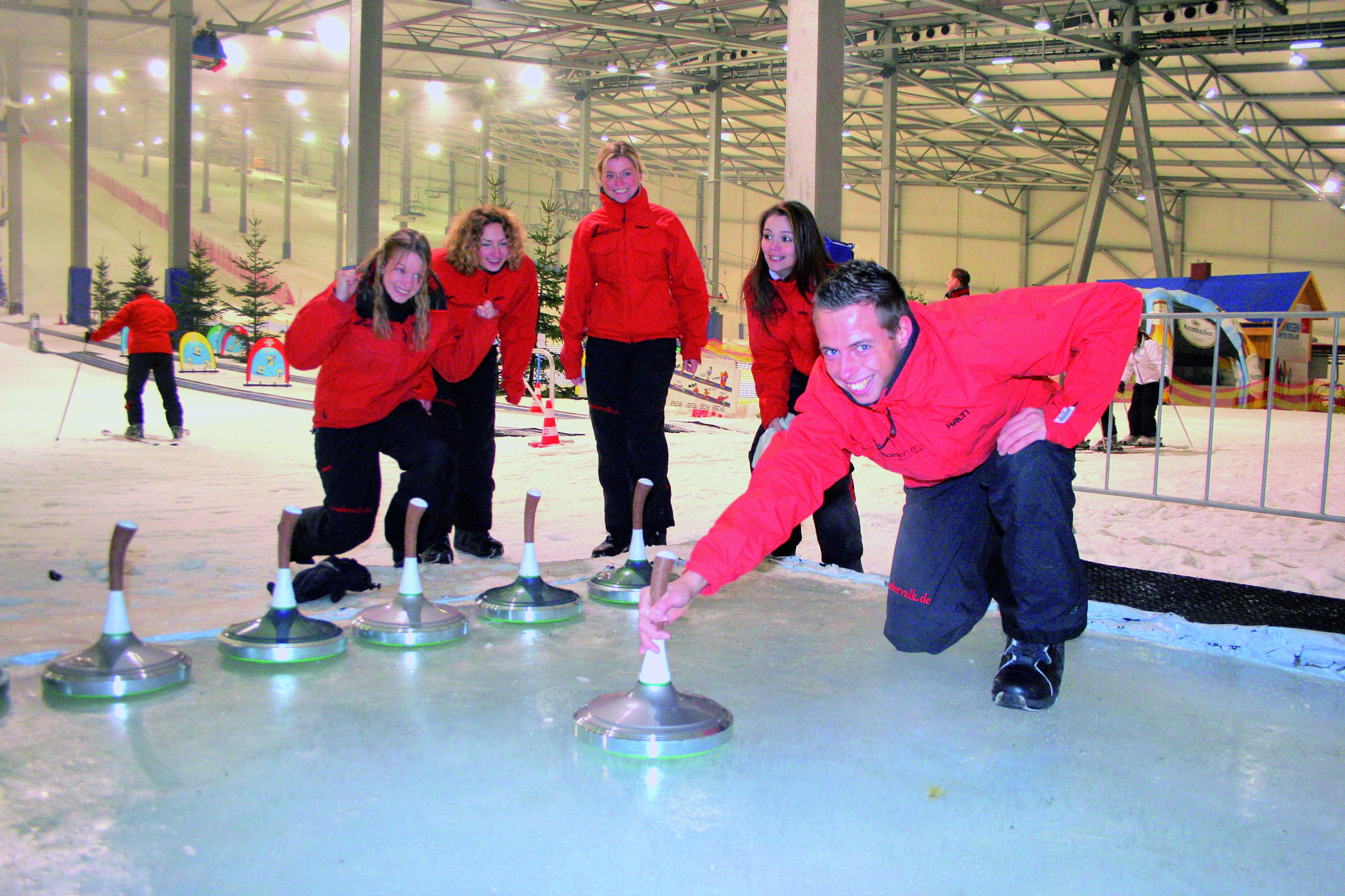 A group of people in red jackets playing curling on an indoor ice rink.