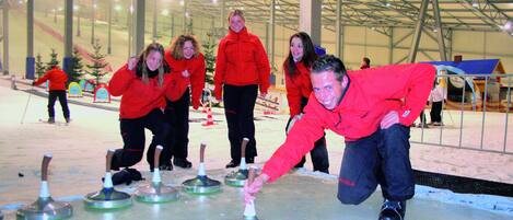 A group of people in red jackets playing curling on an indoor ice rink.