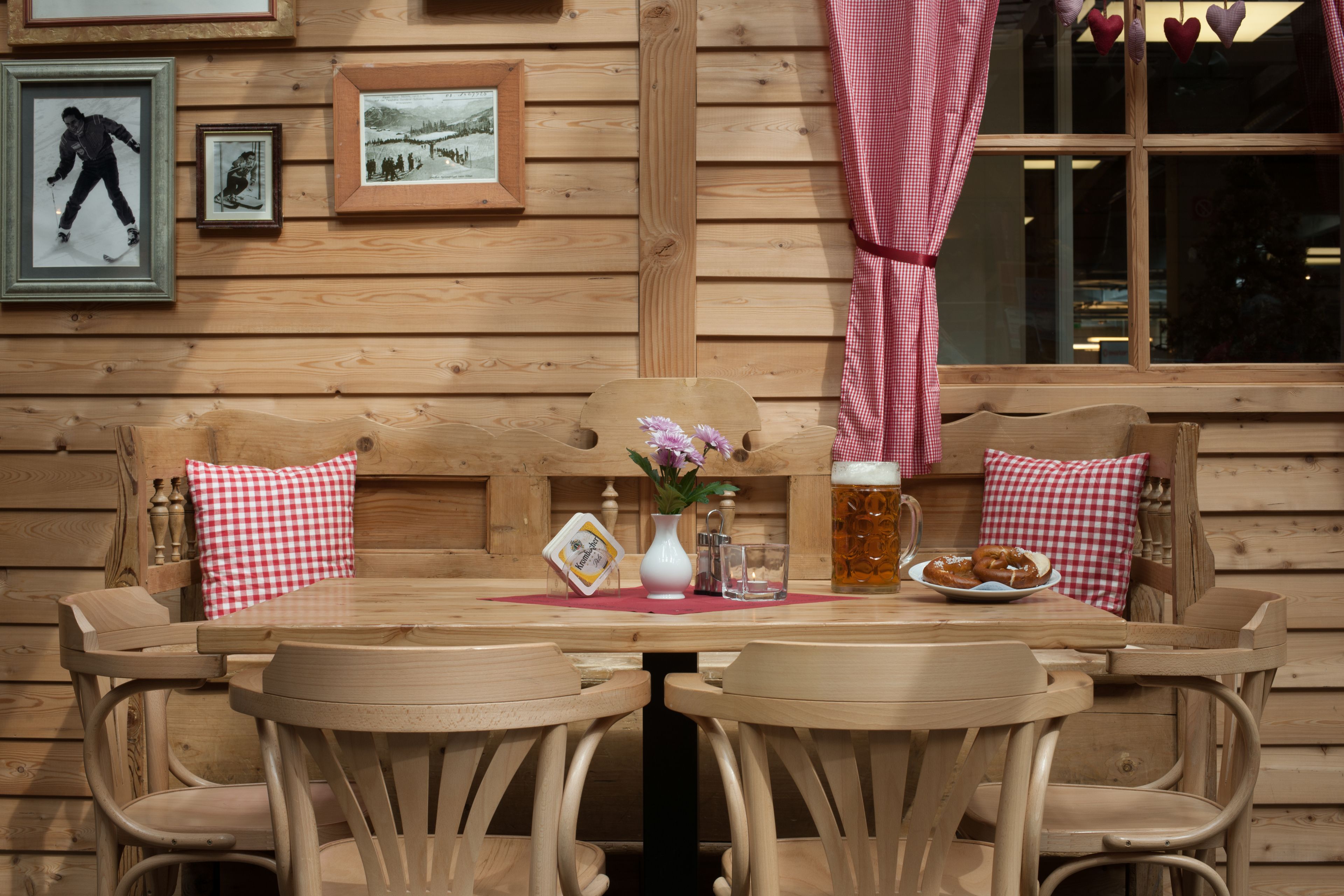 Interieur van een houten chalet met een eettafel, stoelen, een vaas met bloemen, een biertje en ingelijste foto's aan de muur.