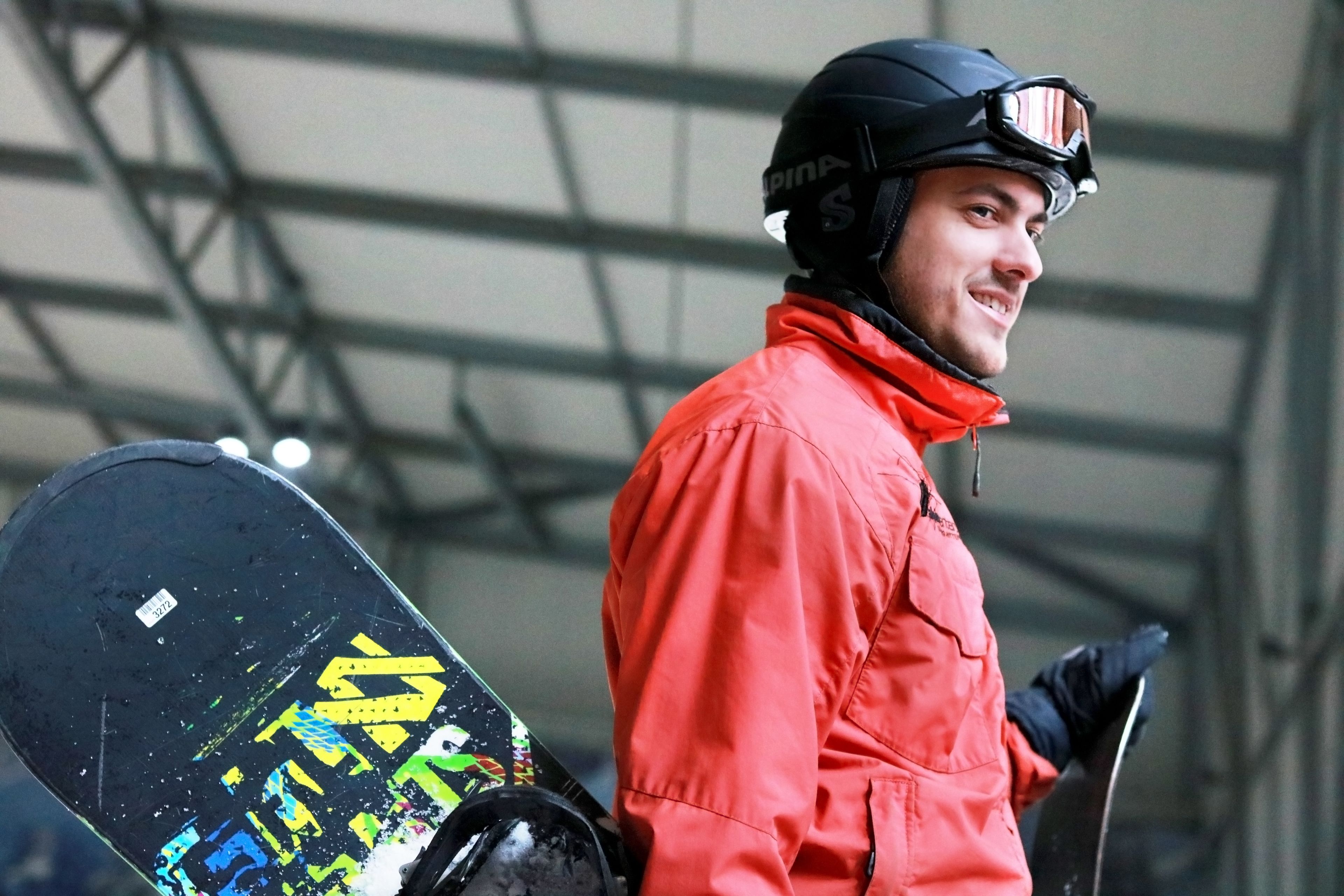 A person in a red jacket holding a snowboard with a colorful design.