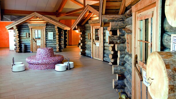 A log cabin interior with a central seating area, wooden beams, and a stone wall.