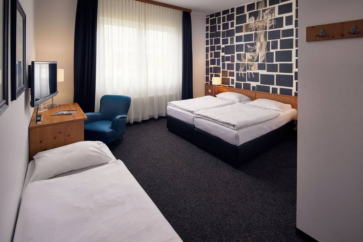 Ein Hotelzimmer mit zwei Betten, einem Schreibtisch mit Fernseher, einem Sessel und einer Wand mit geometrischem Muster.