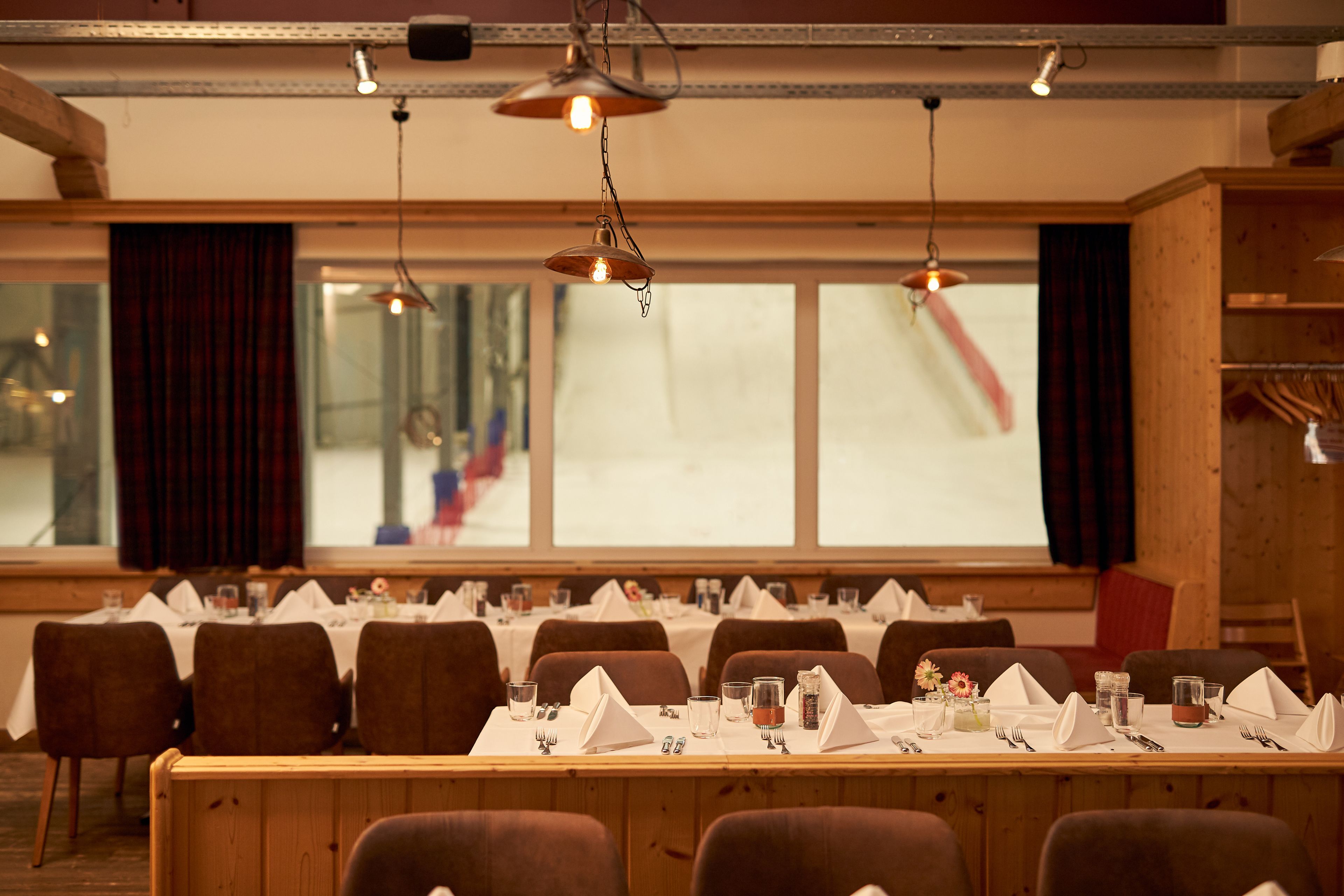 A dining area with tables set for a meal, chairs, and hanging pendant lights.